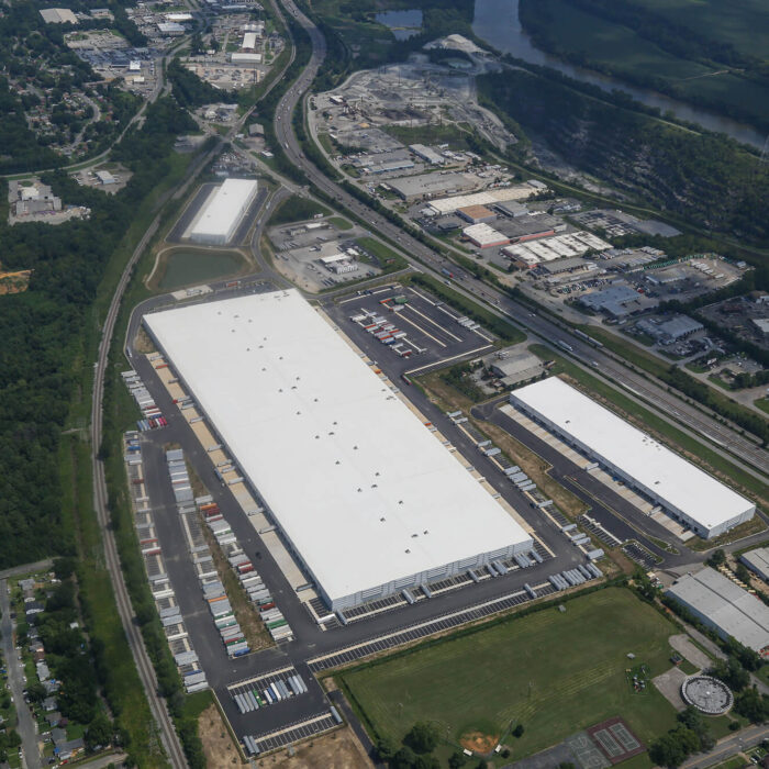 Aerial view: large warehouse complex, white roofs, docks, river nearby.