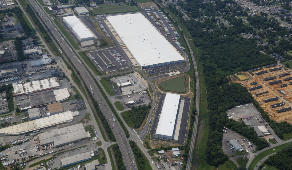 Aerial view: warehouses, parking lots, roads, green spaces, homes.