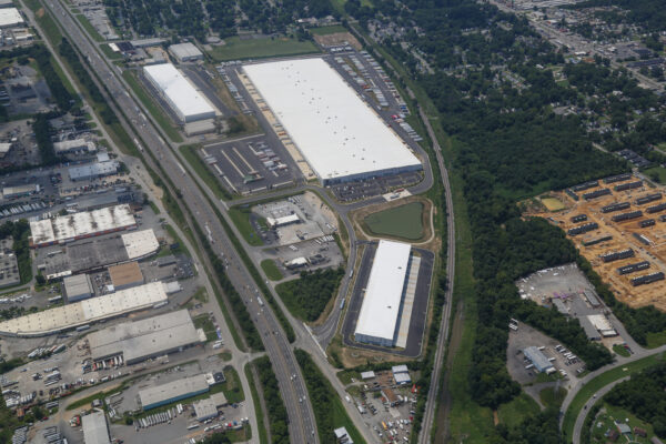 Aerial view: warehouses, parking lots, roads, green spaces, homes.