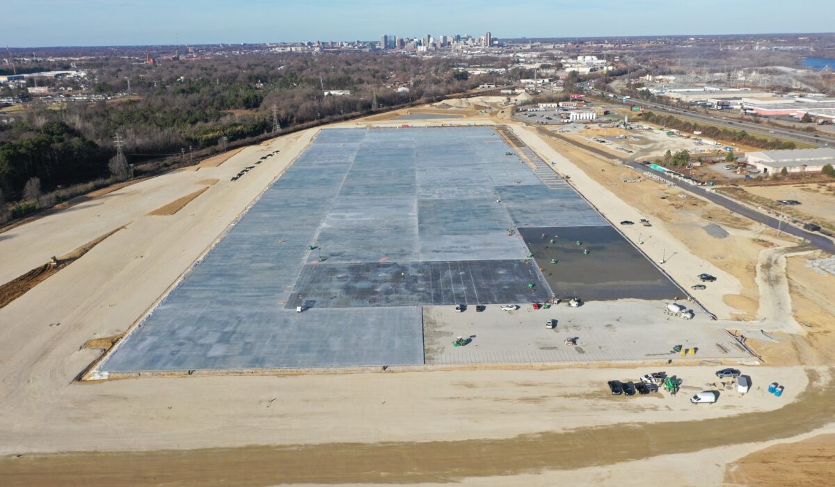 Construction site with concrete foundation, dirt, vehicles, city skyline.