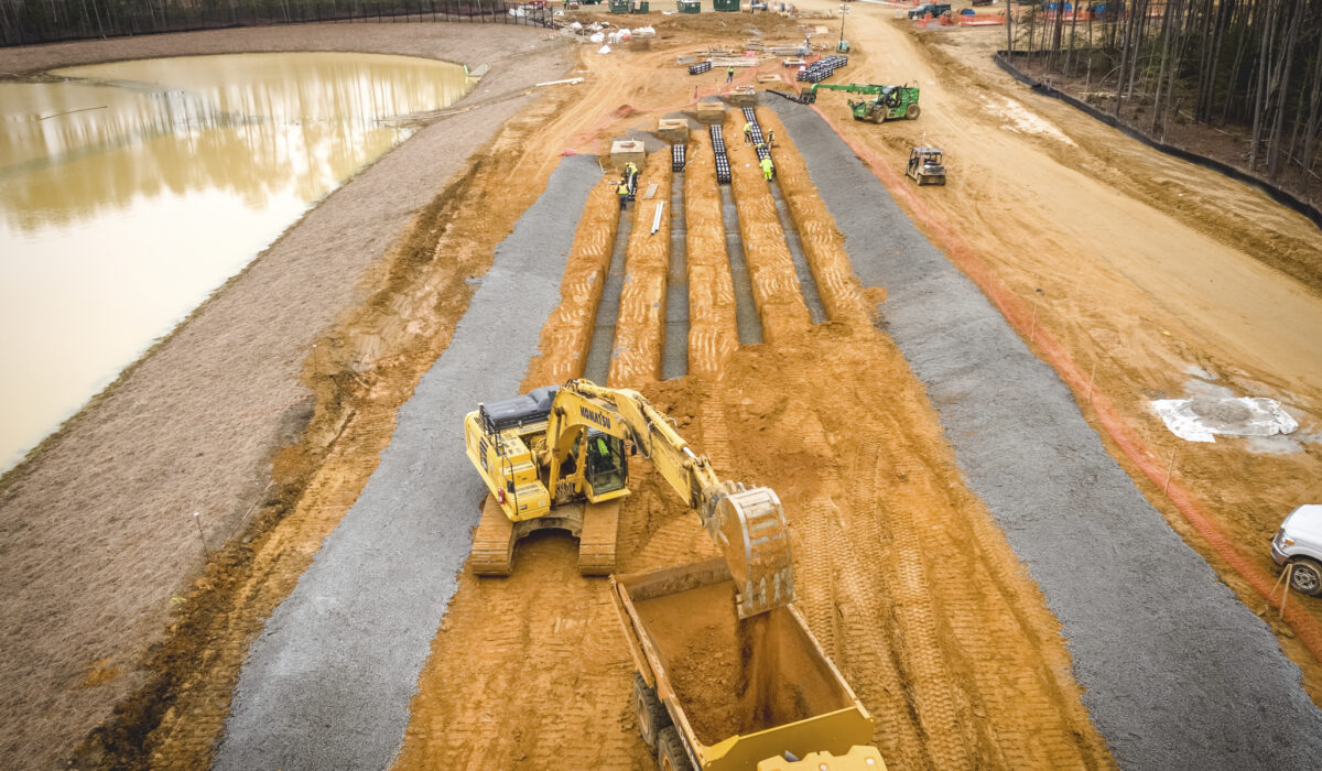 Heavy machinery digging and moving soil near pond and woods.
