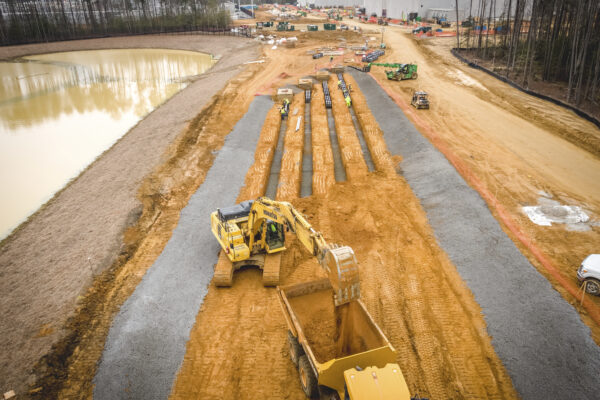 Heavy machinery digging and moving soil near pond and woods.