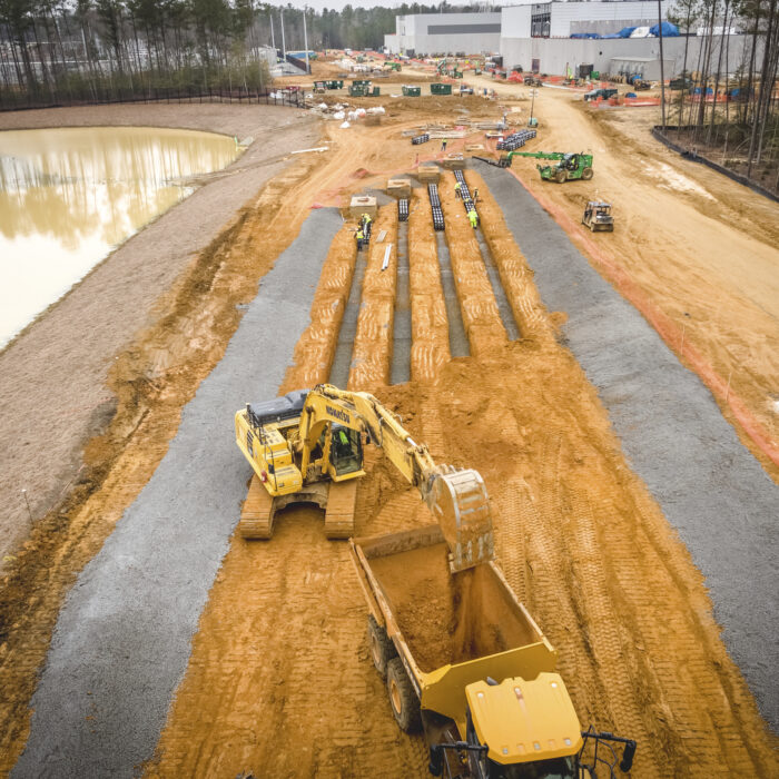 Heavy machinery digging and moving soil near pond and woods.