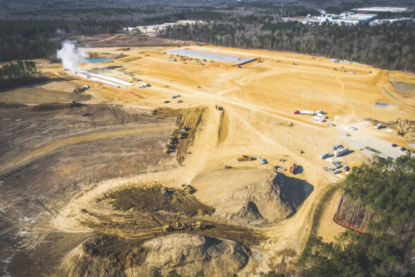 Aerial of construction site, vehicles, machinery, steam, forest edge.