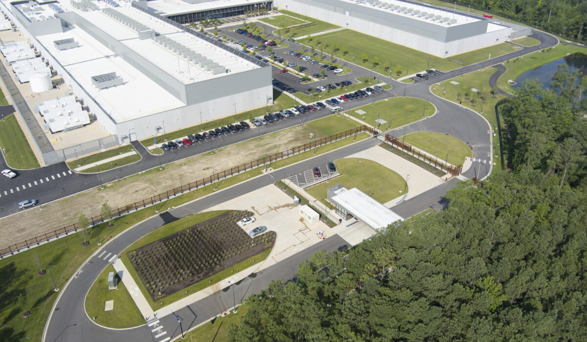 Aerial view of large industrial complex beside wooded area.