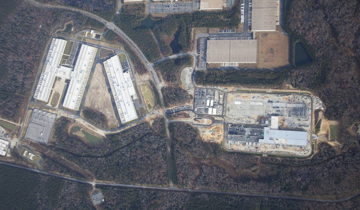 Aerial view of warehouses, parking lots, construction, and woods.