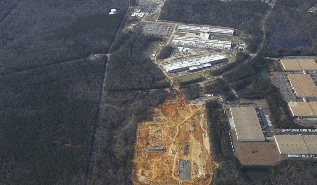 Aerial view: construction site, forest, nearby factories.