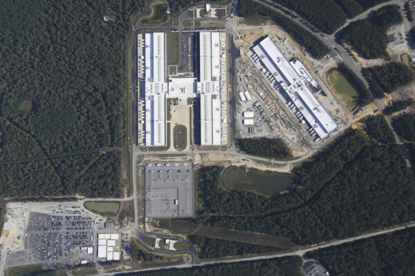 Aerial view of large industrial complex amid forested area.