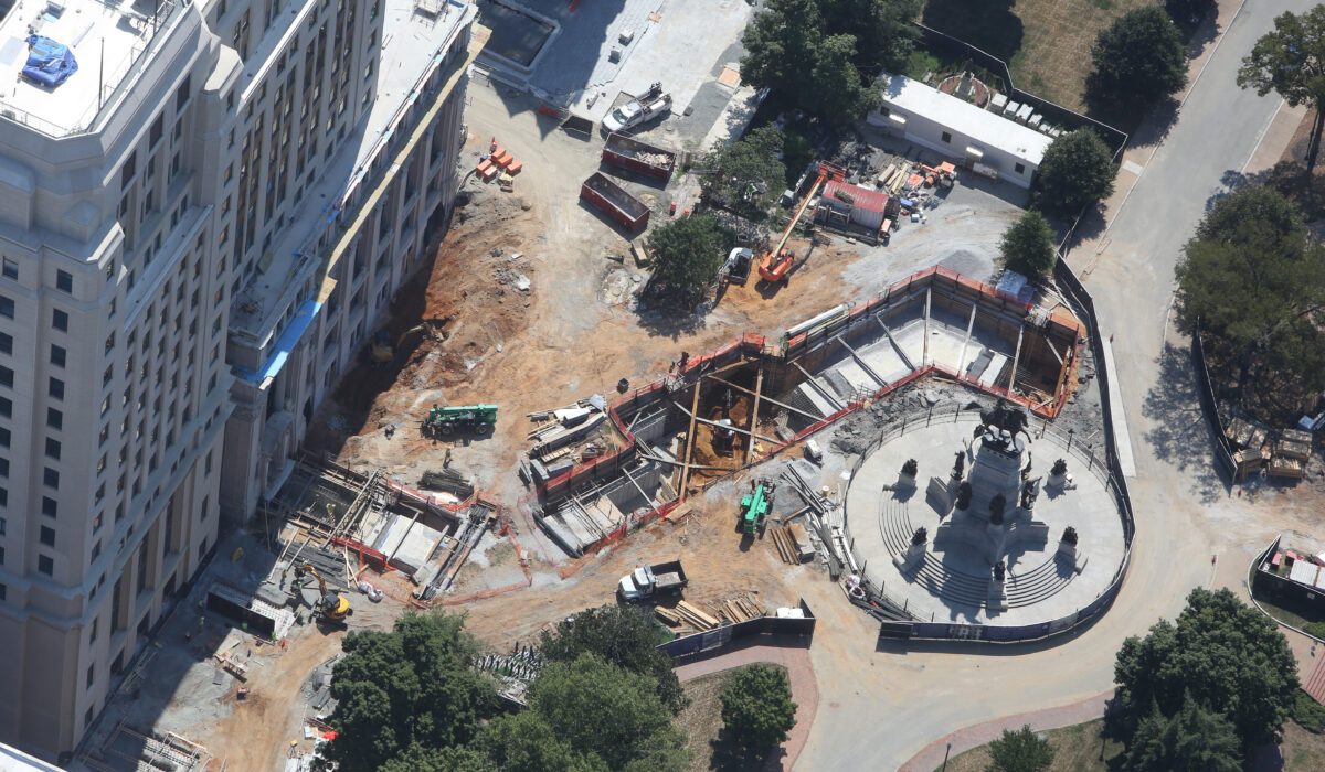 Aerial view: construction site beside large building and circular monument.