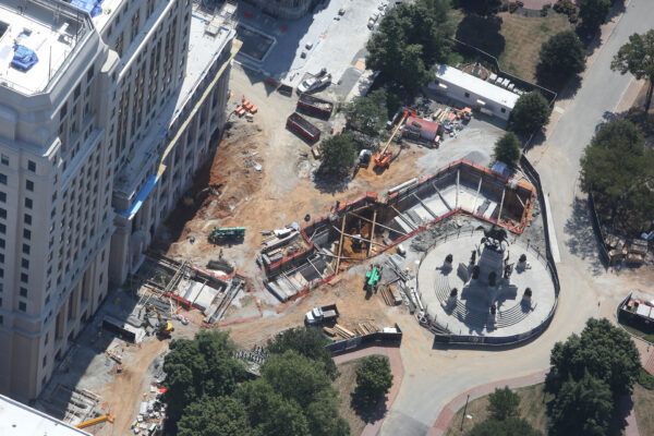Aerial view: construction site beside large building and circular monument.