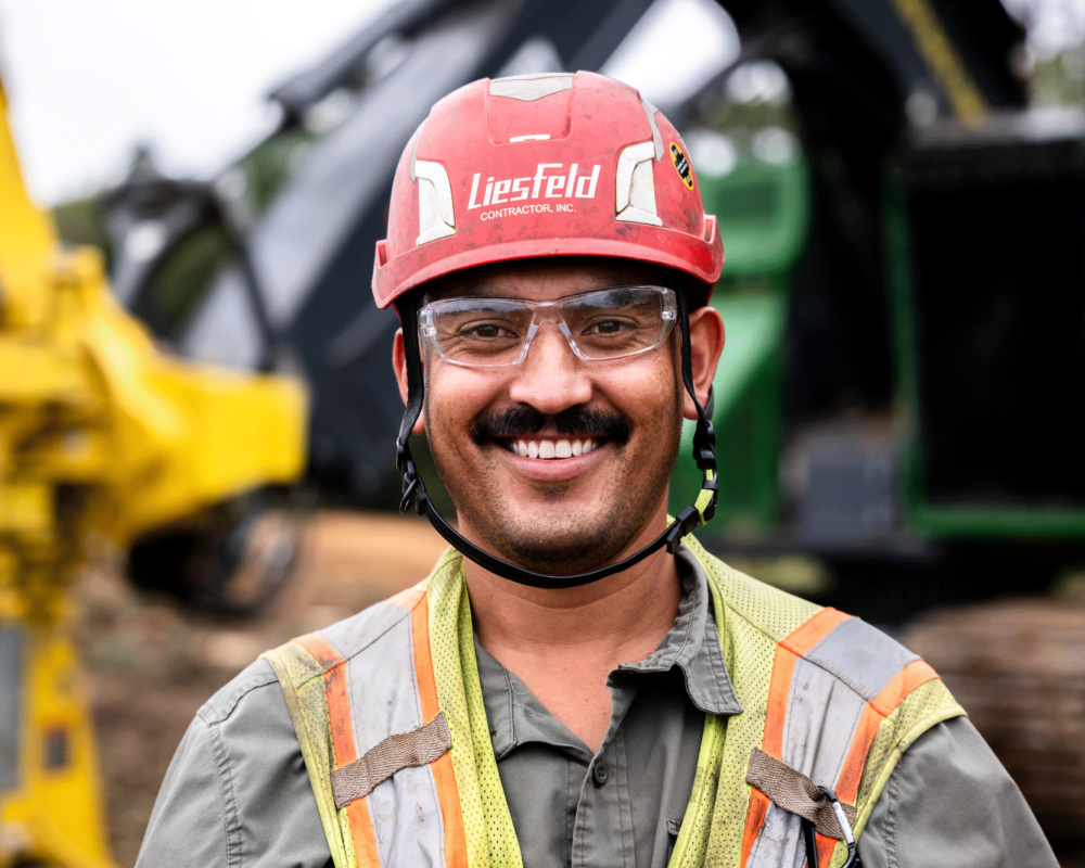 Smiling construction worker in safety gear stands outdoors by machinery.