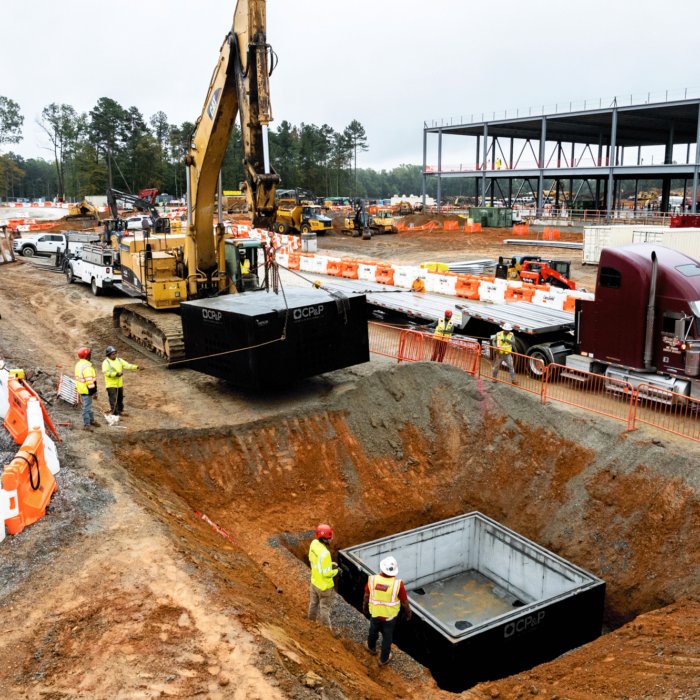 Workers guide an excavator lowering concrete at a busy site.