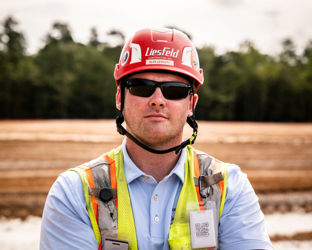 Construction worker in red helmet and vest stands outdoors.