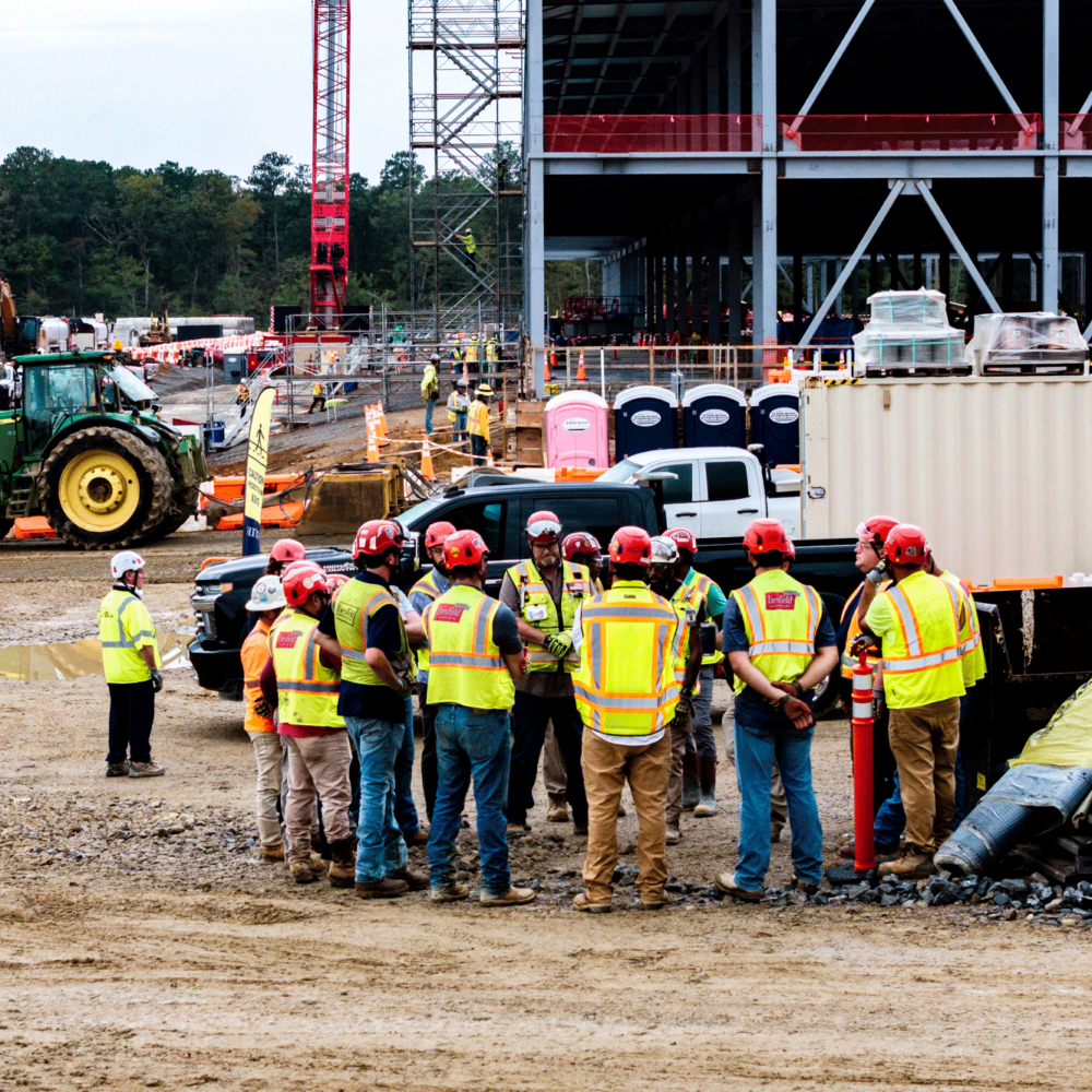 Construction workers in safety gear meet at active site.
