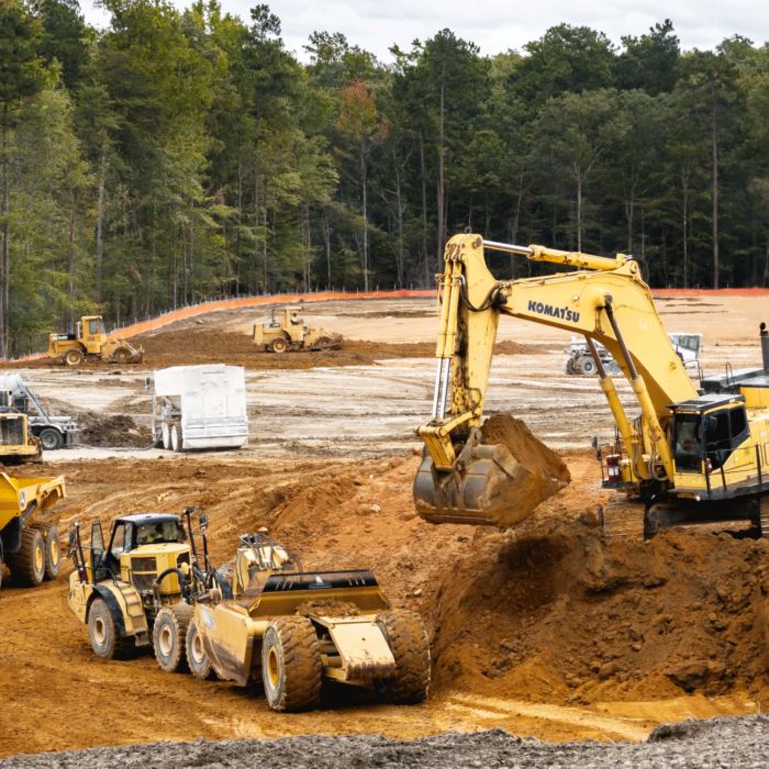 Excavator loads soil into dump truck at busy construction site.
