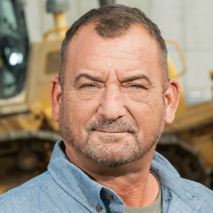 Man with beard stands by construction equipment.