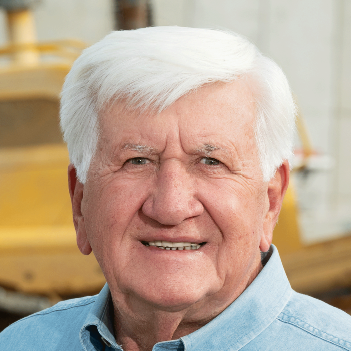 Smiling man in blue shirt, construction equipment behind.