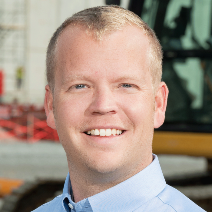 Man in blue shirt smiles near construction equipment.