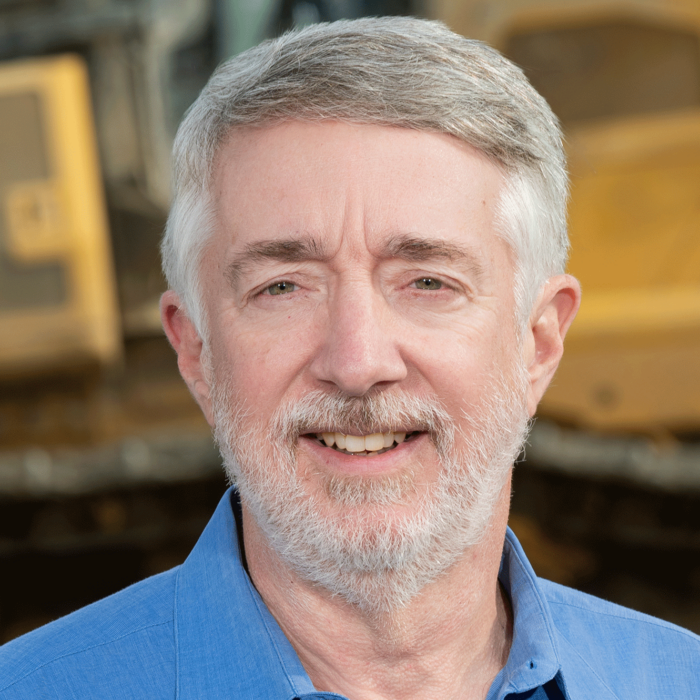 Man with beard in blue shirt stands by construction.