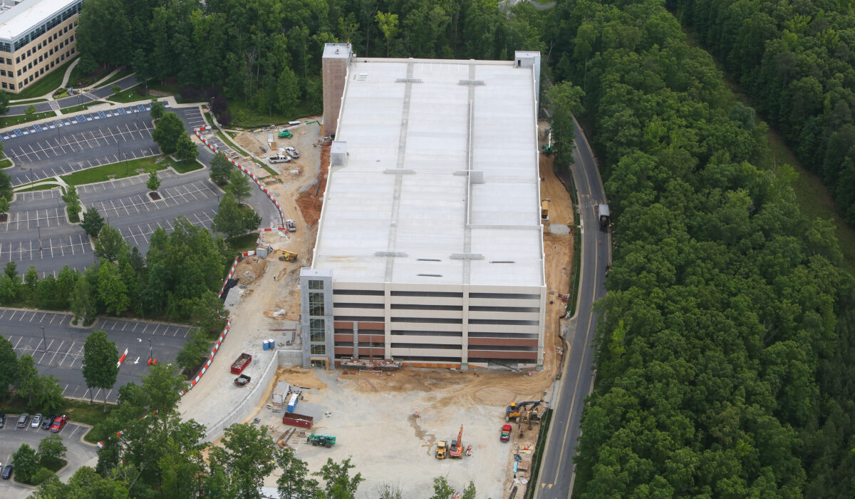 Aerial view: multi-level parking garage under construction near trees.