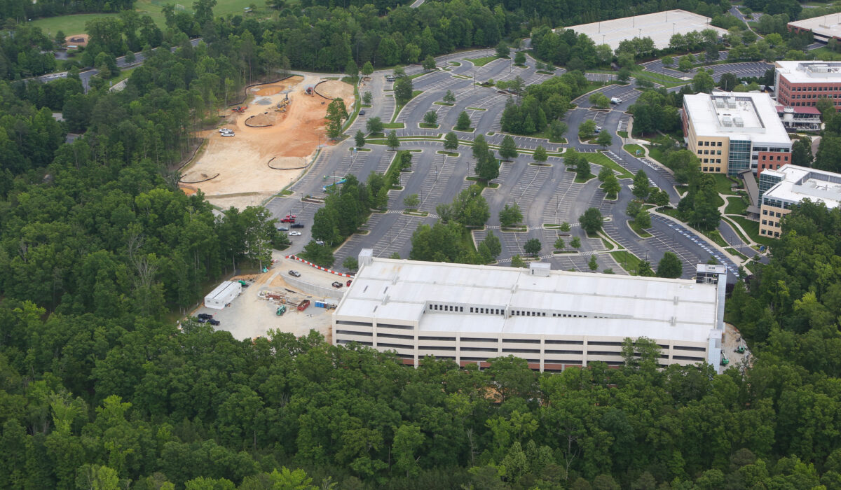 Aerial view: sparse parking, office buildings, construction, green trees.