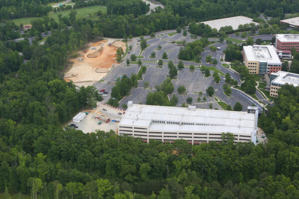 Aerial view: sparse parking, office buildings, construction, green trees.