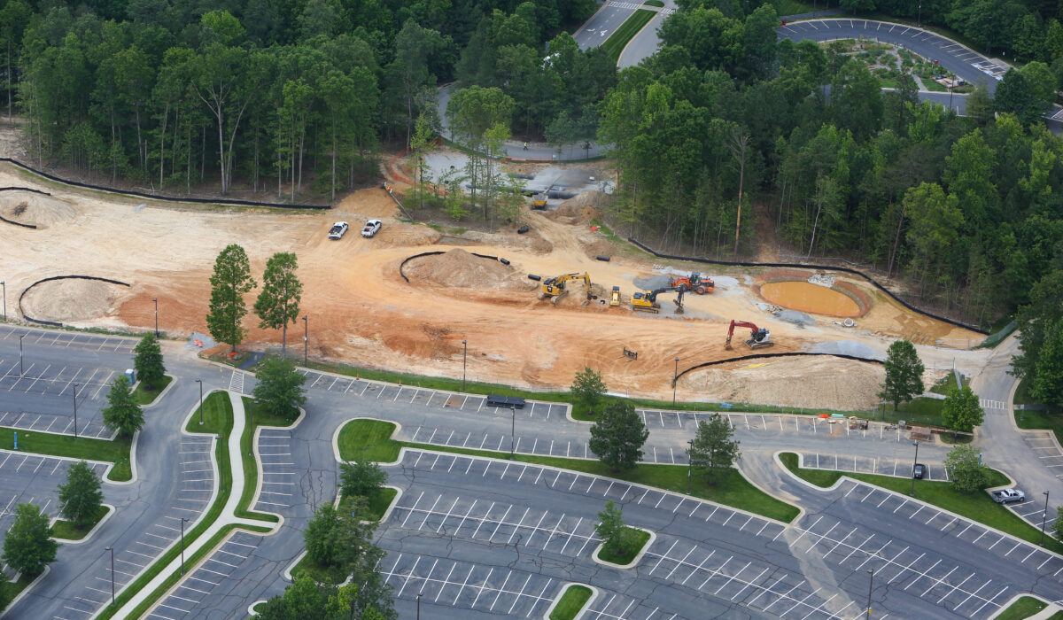 Aerial view: construction site, machinery, empty lot, surrounding trees.