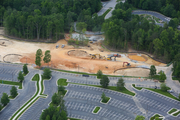 Aerial view: construction site, machinery, empty lot, surrounding trees.