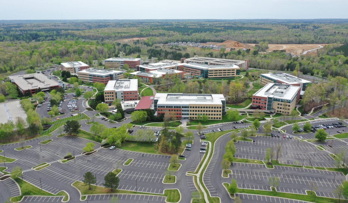Aerial view: office complex, multiple buildings, greenery, empty parking.