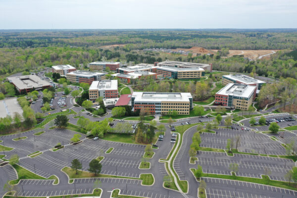 Aerial view: office complex, multiple buildings, greenery, empty parking.