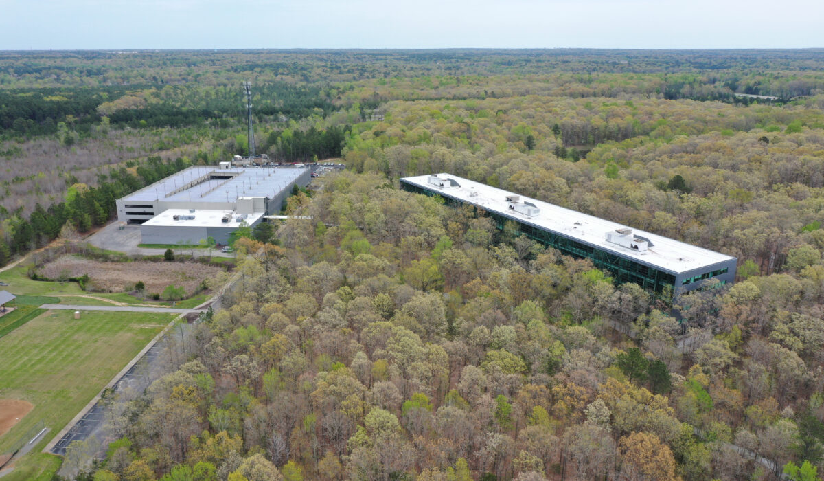 Aerial view: two office buildings, dense forest, parking, baseball.