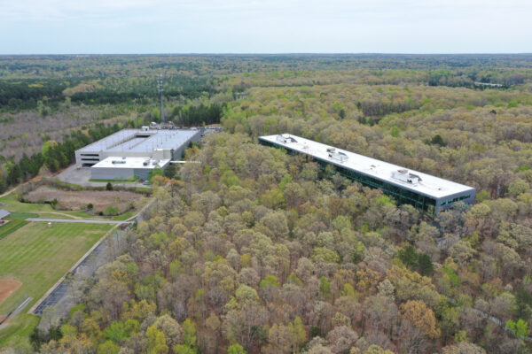 Aerial view: two office buildings, dense forest, parking, baseball.