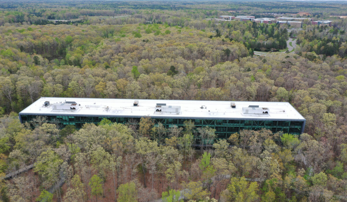 Large white-roofed building amid forest, distant buildings visible.