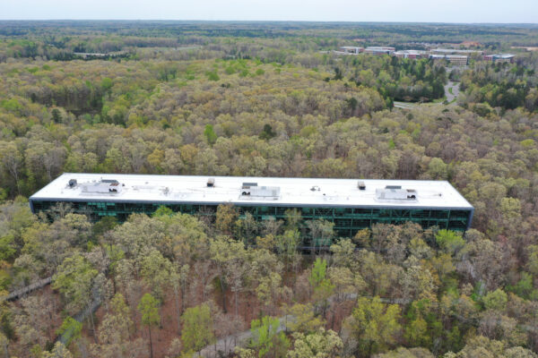 Large white-roofed building amid forest, distant buildings visible.