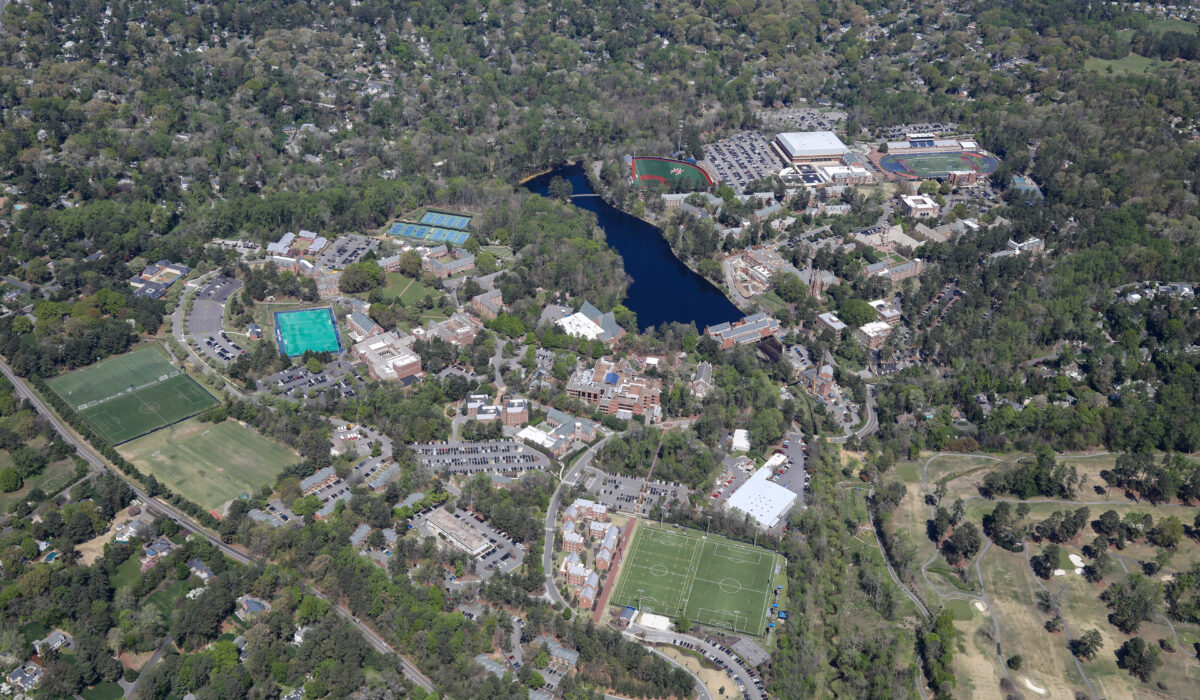 Aerial view: campus with buildings, fields, lake, greenery.