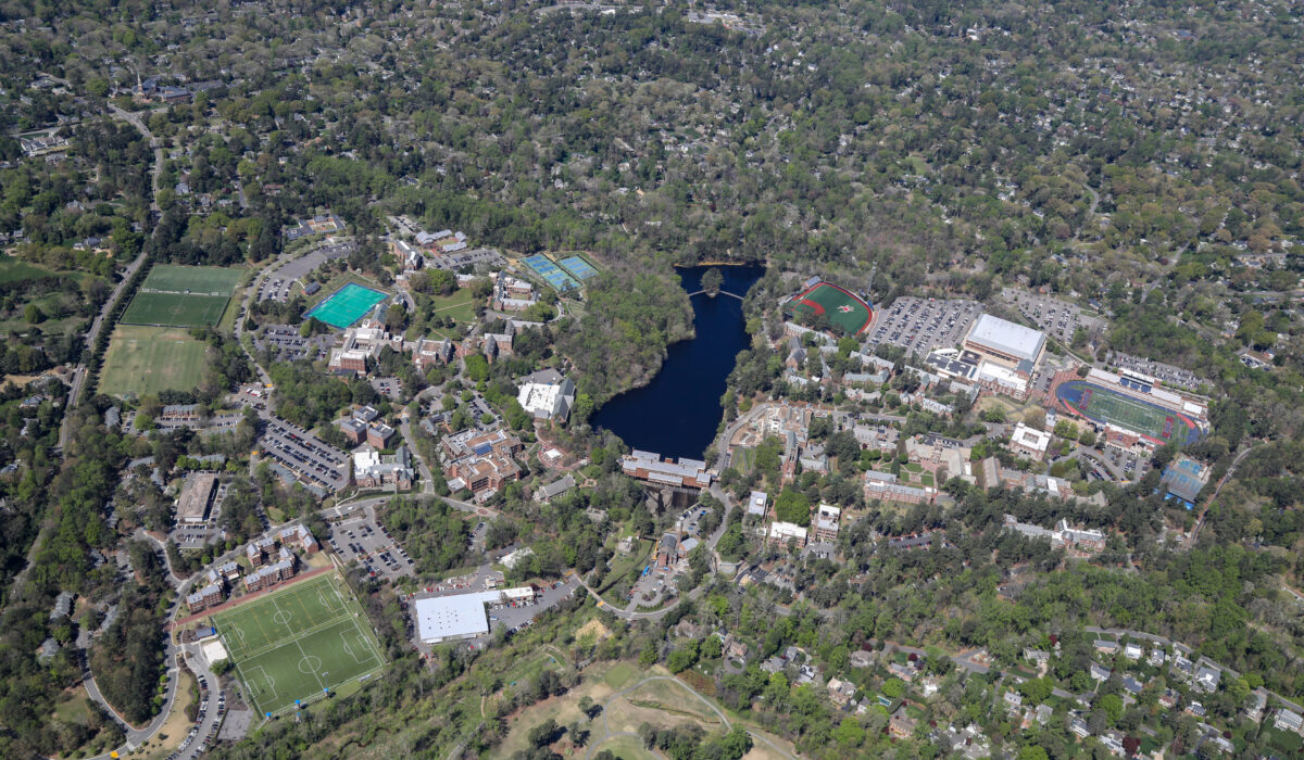 Aerial view: campus with sports fields, pond, trees, houses.