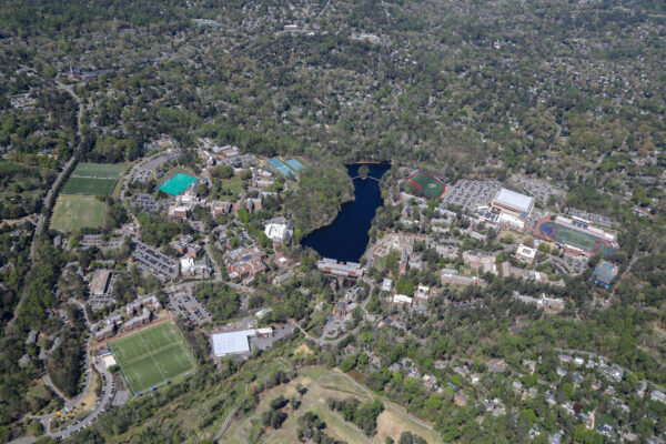 Aerial view: campus with sports fields, pond, trees, houses.