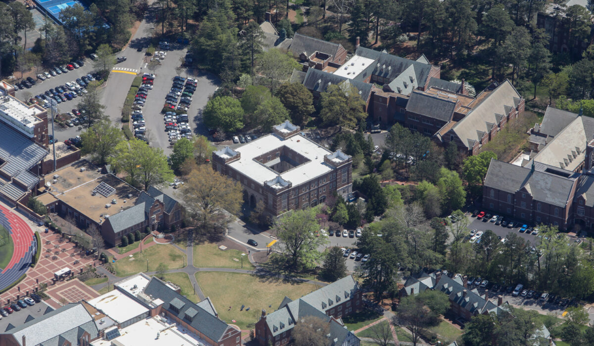 Aerial view: brick campus buildings, parking lots, grass, trees.