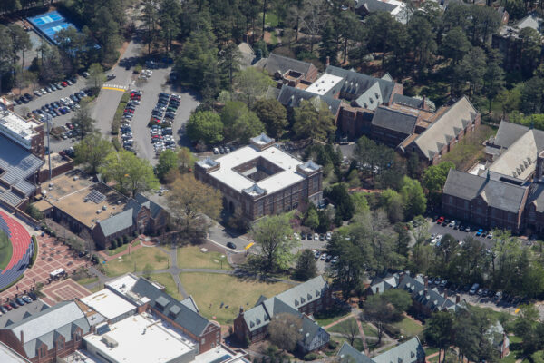 Aerial view: brick campus buildings, parking lots, grass, trees.