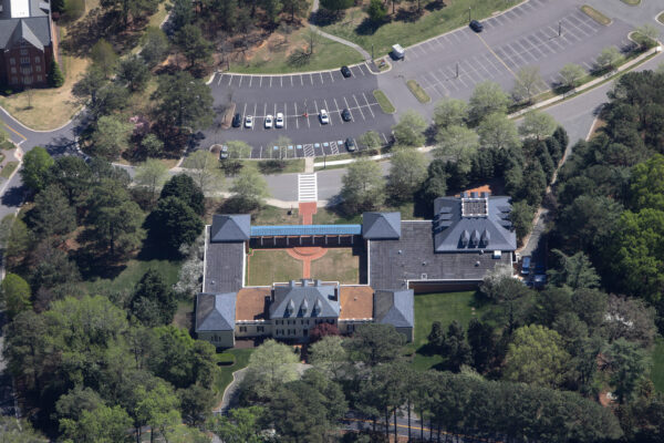 Aerial view: building with courtyard, trees, parking lot, cars.