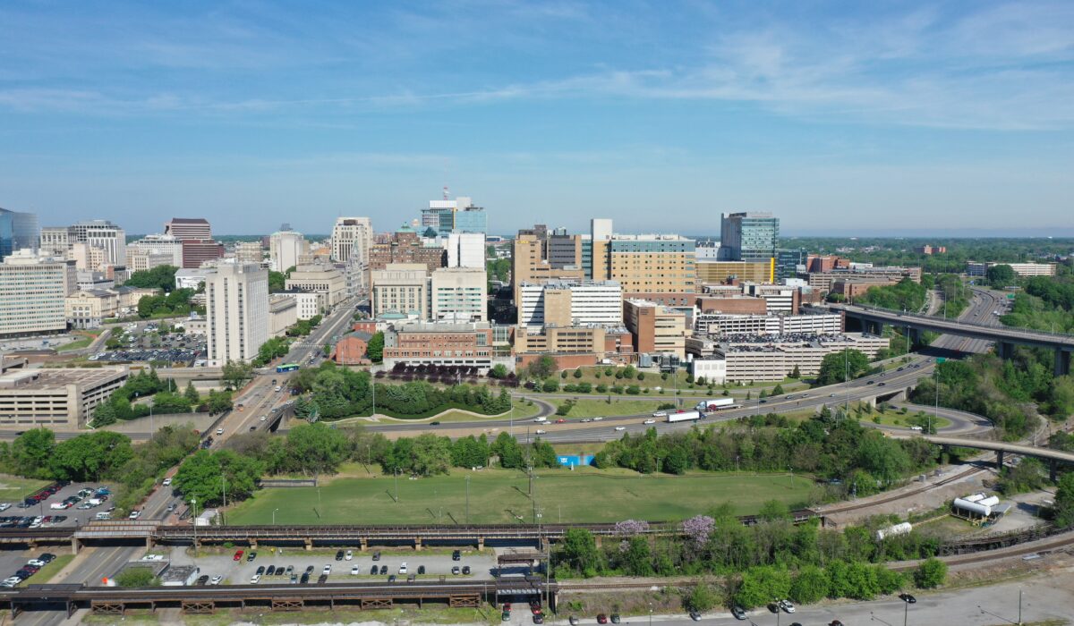 Aerial cityscape: tall buildings, highways, green spaces, blue sky.