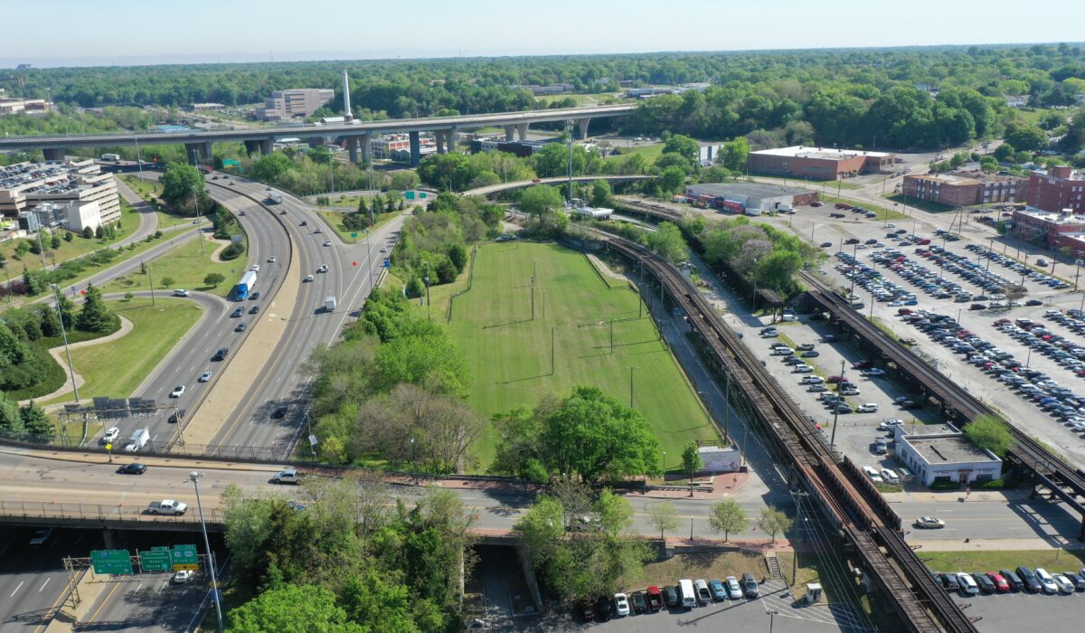 Aerial view: highway, railway, grassy park, parking lots, buildings.