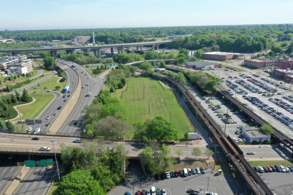 Aerial view: highway, railway, grassy park, parking lots, buildings.