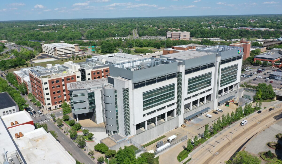 Aerial view of modern hospital, trees, parking lots, and buildings.