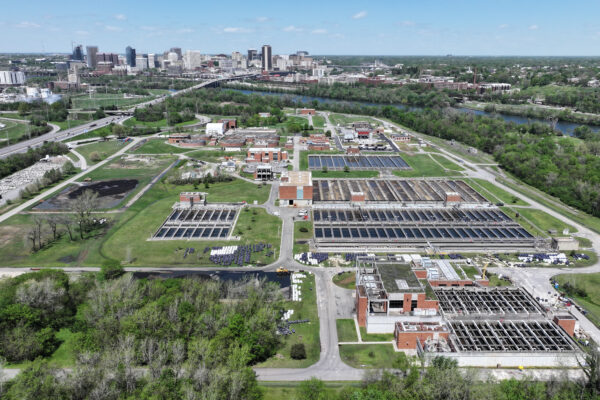 Aerial view: water treatment plant, greenery, city skyline, clear sky.