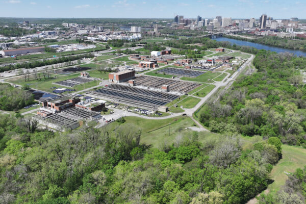 Aerial view: water treatment plant, trees, city skyline, river.