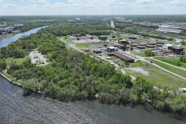 River flanked by green forest and brown buildings, industry beyond.