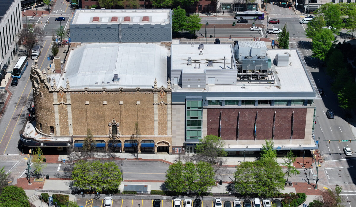 Aerial view: historic theater, modern building, cars, tree-lined street.