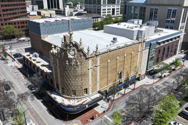 Aerial view: ornate historic theater amid modern buildings and trees.