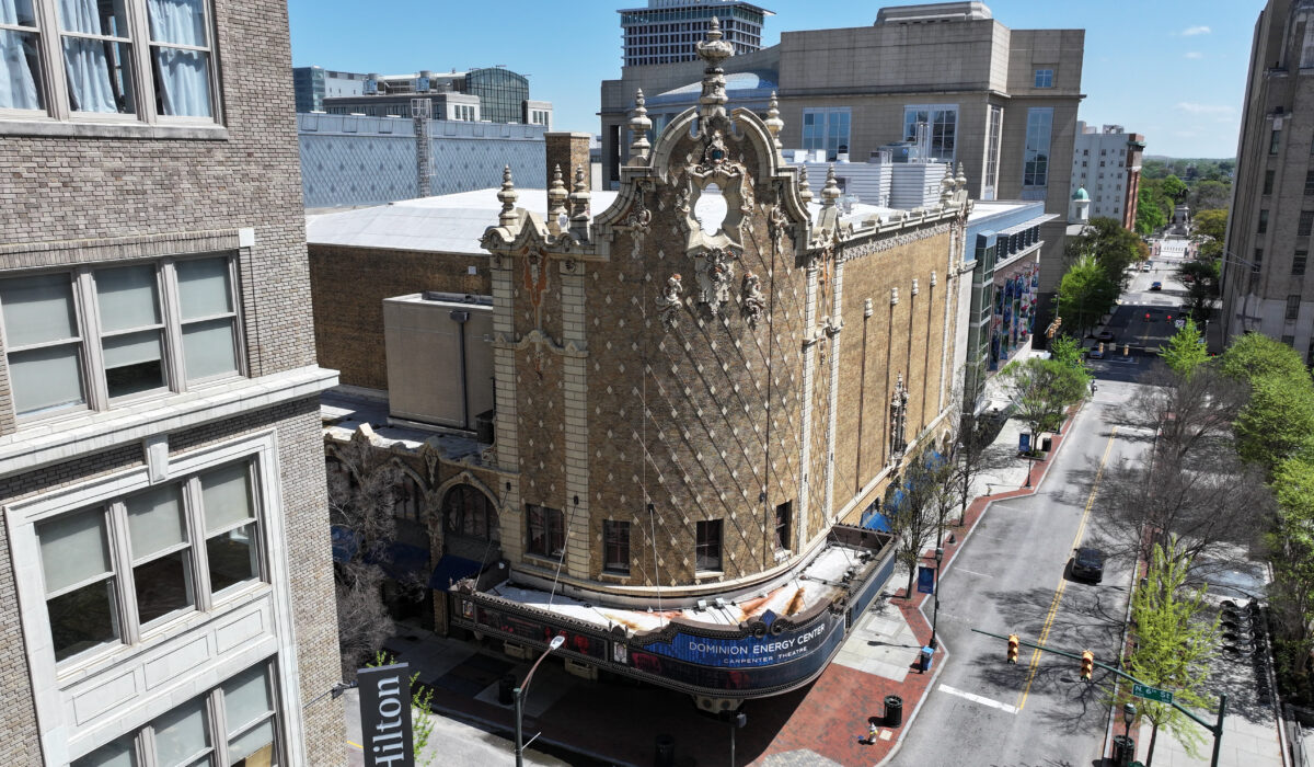 Ornate historic theater stands amid modern buildings on sunny day.